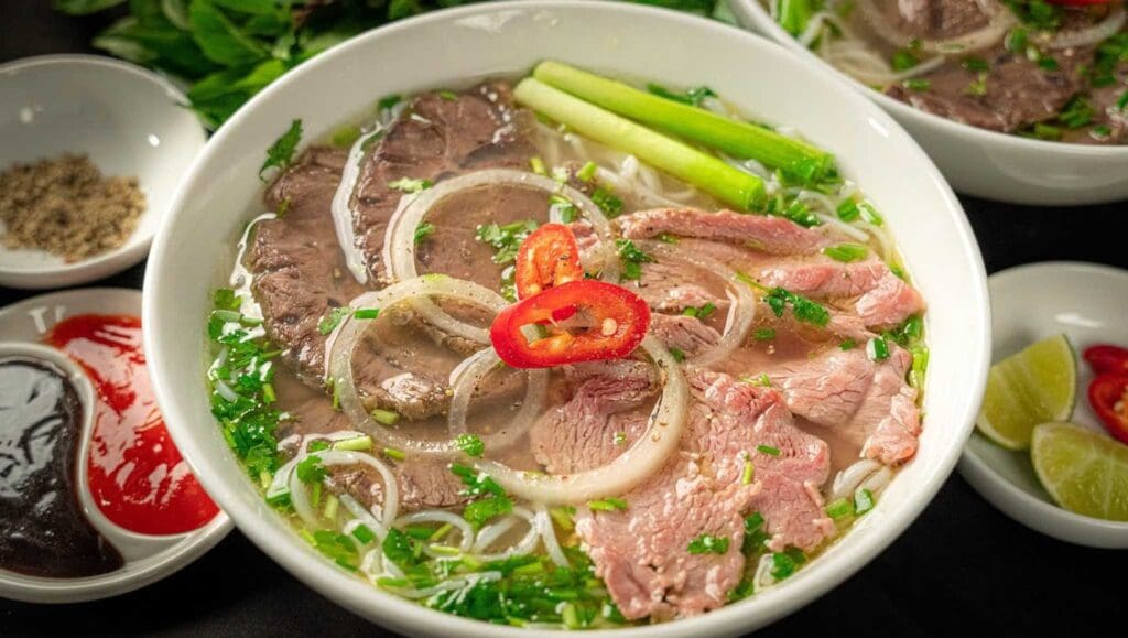 Authentic Vietnamese Pho in Saigon – hearty beef noodle soup with rare beef slices, brisket, fresh herbs, onions, and rich aromatic broth.